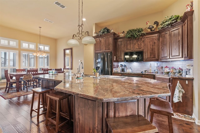 kitchen with visible vents, stainless steel refrigerator with ice dispenser, a kitchen breakfast bar, backsplash, and black microwave