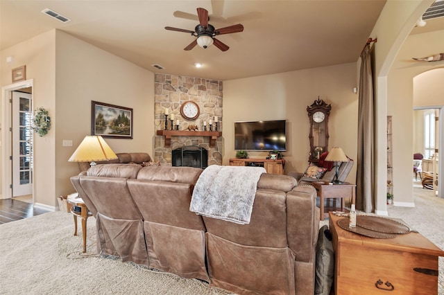 living room featuring arched walkways, a stone fireplace, visible vents, and ceiling fan