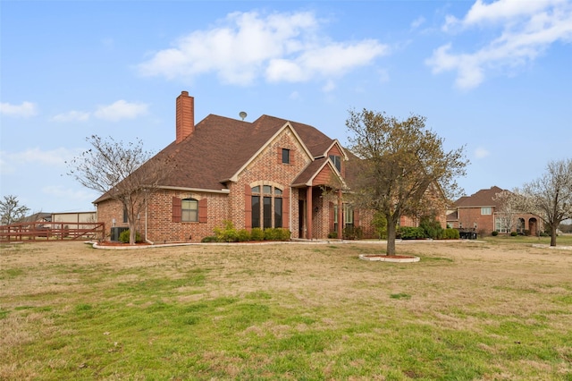 french country home with brick siding, a chimney, a front yard, and a shingled roof