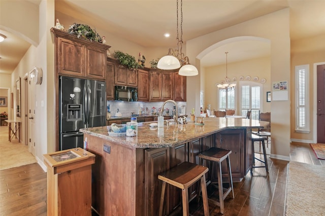 kitchen featuring a center island with sink, tasteful backsplash, stainless steel fridge, arched walkways, and black microwave