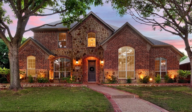 view of front facade with stone siding, brick siding, a lawn, and roof with shingles