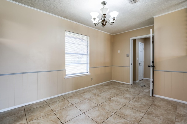 empty room featuring a wainscoted wall, light tile patterned flooring, ornamental molding, a textured ceiling, and a notable chandelier