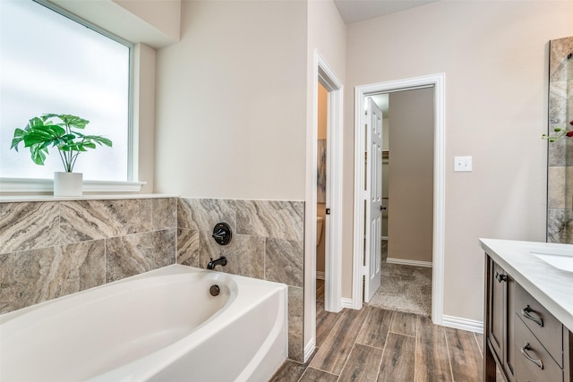 bathroom with wood finished floors, vanity, baseboards, and a bath