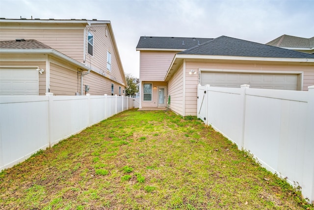 back of property featuring a yard, a shingled roof, an attached garage, and fence