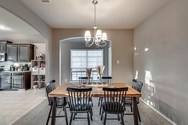 dining space with light tile patterned floors, baseboards, arched walkways, light colored carpet, and a chandelier