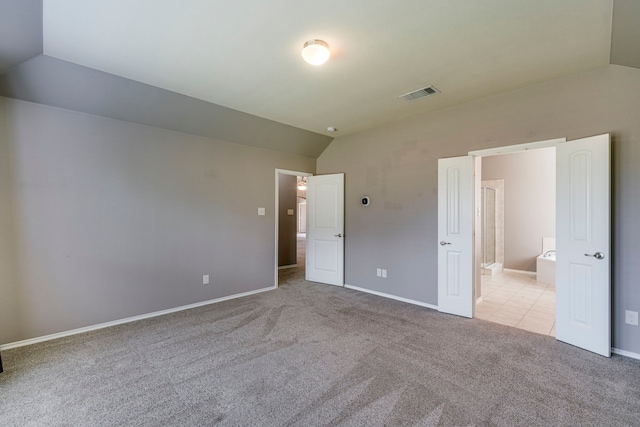 unfurnished bedroom with lofted ceiling, ensuite bathroom, carpet flooring, visible vents, and baseboards