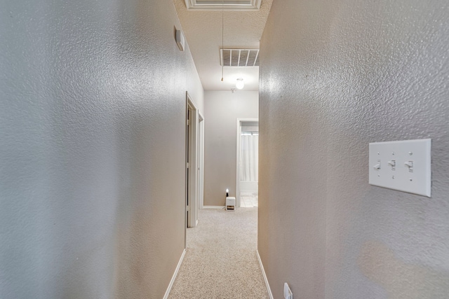 hallway with visible vents, a textured wall, carpet, and attic access