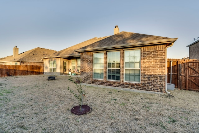 back of property featuring roof with shingles, a chimney, fence, and brick siding