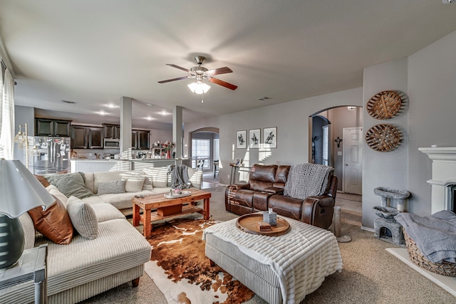 living room with arched walkways, visible vents, light carpet, ceiling fan, and baseboards