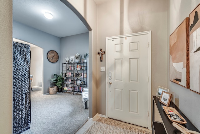 entrance foyer with arched walkways, light carpet, and baseboards