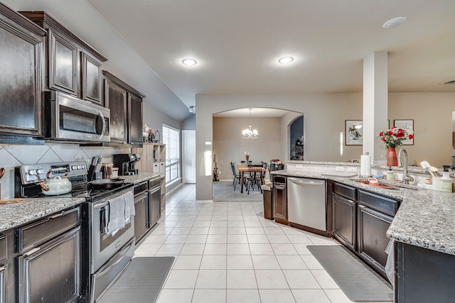 kitchen featuring dark brown cabinetry, light tile patterned floors, arched walkways, appliances with stainless steel finishes, and a sink