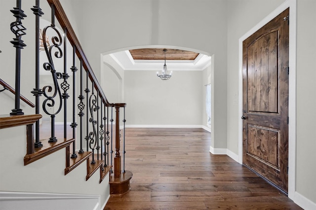 foyer with baseboards, arched walkways, dark wood-type flooring, a tray ceiling, and crown molding