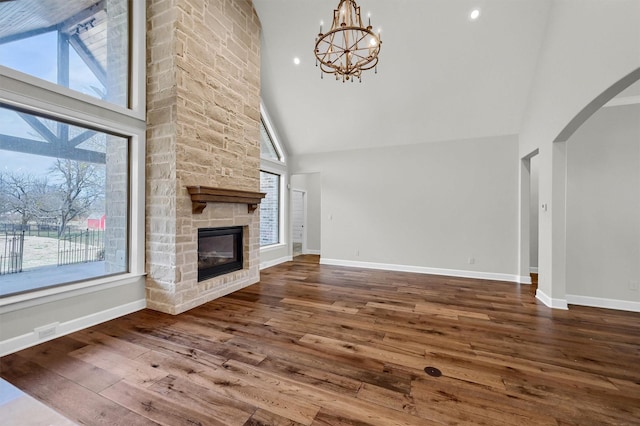 unfurnished living room with arched walkways, a stone fireplace, hardwood / wood-style flooring, and baseboards