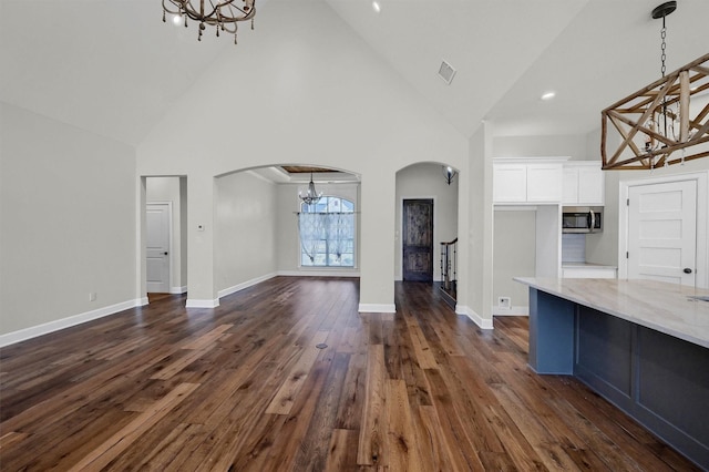 unfurnished living room featuring arched walkways, high vaulted ceiling, baseboards, dark wood-style floors, and an inviting chandelier