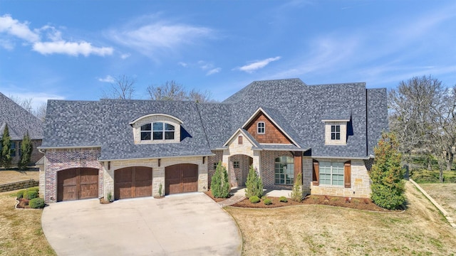 french country inspired facade with a shingled roof, a garage, stone siding, driveway, and a front lawn