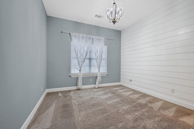 empty room with a chandelier, wooden walls, visible vents, baseboards, and carpet