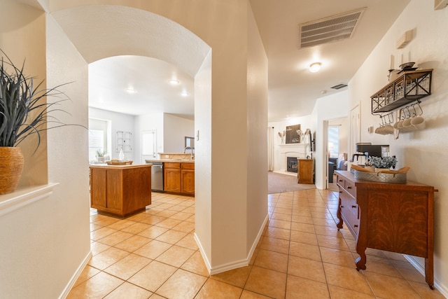 hallway featuring light tile patterned floors, baseboards, visible vents, arched walkways, and a sink