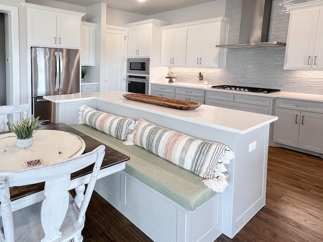 kitchen featuring dark wood-style flooring, light countertops, appliances with stainless steel finishes, white cabinetry, and wall chimney exhaust hood