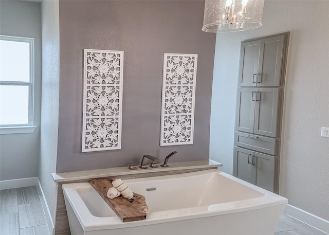 full bath with a bath, a chandelier, and baseboards