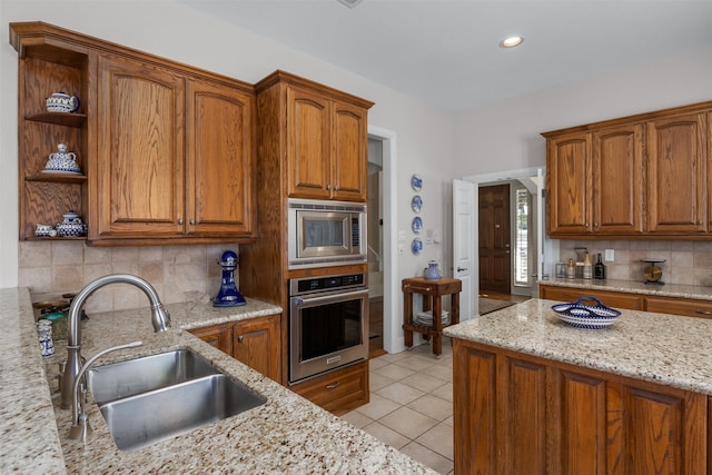 kitchen with light tile patterned floors, appliances with stainless steel finishes, brown cabinets, and a sink