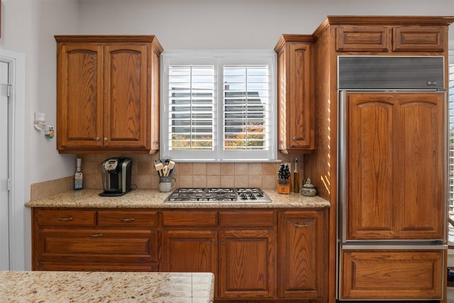 kitchen with brown cabinets, stainless steel gas stovetop, paneled fridge, and decorative backsplash