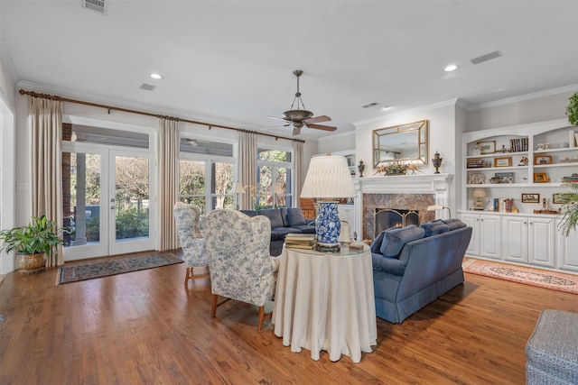 living area with visible vents, ornamental molding, a high end fireplace, and light wood-style flooring