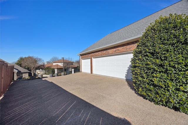 view of home's exterior with brick siding, roof with shingles, concrete driveway, fence, and a garage