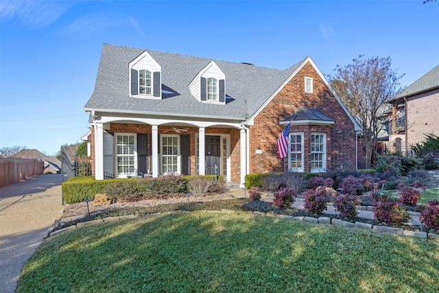 view of front of home with a porch, brick siding, a shingled roof, fence, and a front yard