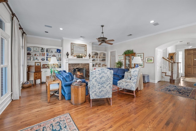 living room with arched walkways, visible vents, ornamental molding, a high end fireplace, and wood finished floors