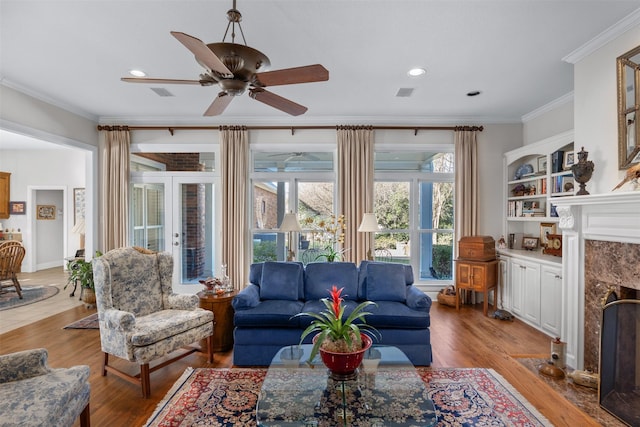 living room featuring light wood finished floors, visible vents, a high end fireplace, ornamental molding, and recessed lighting