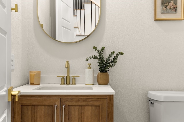 bathroom featuring toilet, a textured wall, and vanity