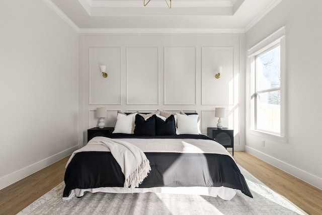 bedroom with baseboards, a tray ceiling, crown molding, light wood-type flooring, and a decorative wall