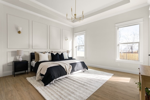 bedroom featuring ornamental molding, an inviting chandelier, a tray ceiling, light wood-type flooring, and a decorative wall