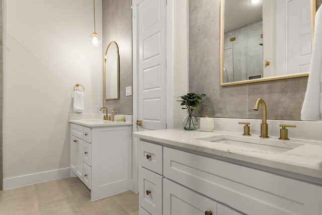 bathroom featuring two vanities, a sink, a tile shower, and baseboards