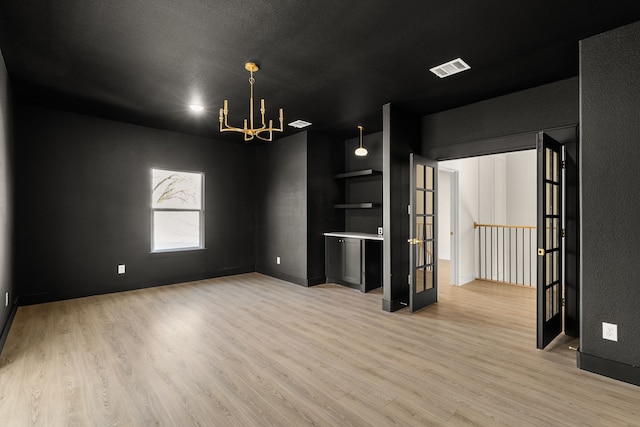 empty room with light wood-type flooring, visible vents, and a chandelier