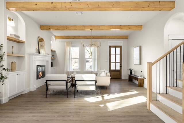 living room with stairs, light wood finished floors, beamed ceiling, and a glass covered fireplace