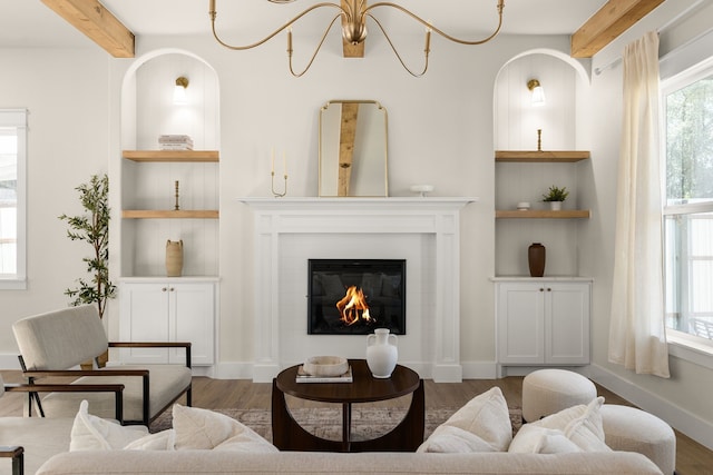 living area featuring built in shelves, beamed ceiling, wood finished floors, and baseboards