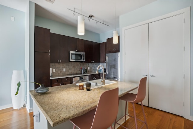 kitchen with dark brown cabinetry, light wood finished floors, tasteful backsplash, stainless steel appliances, and a sink