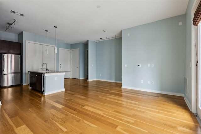 unfurnished living room featuring a sink, light wood finished floors, visible vents, and baseboards