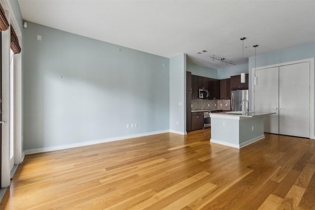 kitchen featuring light wood finished floors, stainless steel appliances, tasteful backsplash, dark brown cabinetry, and an island with sink