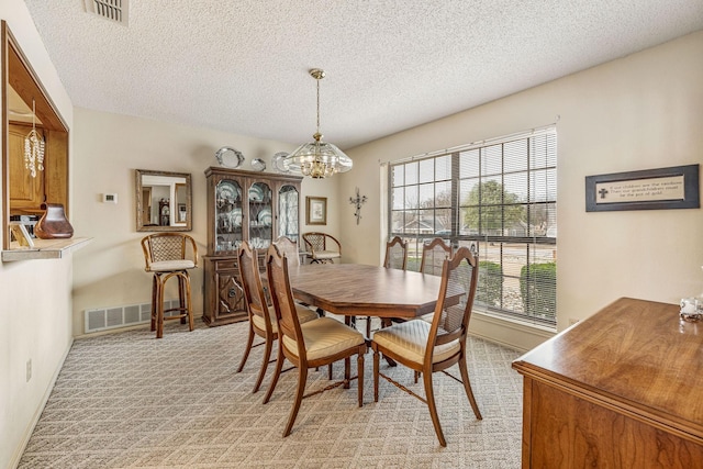 dining space with visible vents, a notable chandelier, light carpet, and a textured ceiling