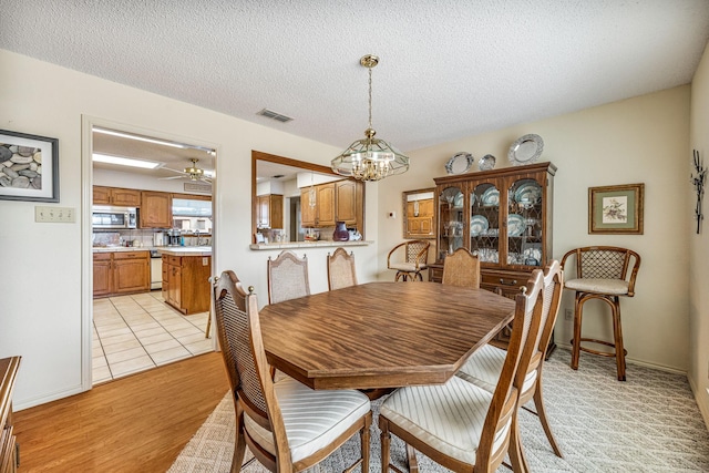 dining area featuring visible vents, a textured ceiling, light wood finished floors, and ceiling fan with notable chandelier