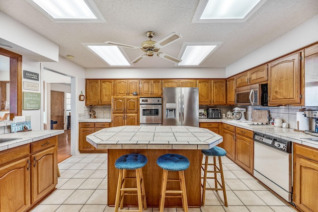 kitchen featuring light tile patterned floors, a kitchen bar, appliances with stainless steel finishes, and brown cabinets