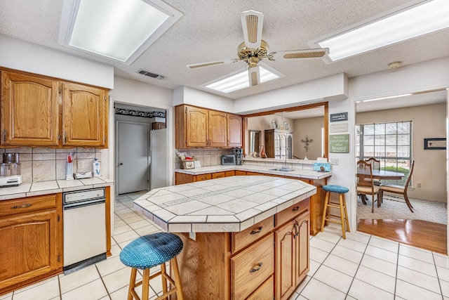 4227 Mojave Dr, Granbury, TX 76049 - kitchen featuring tile counters, decorative backsplash, light tile patterned floors, brown cabinetry, and a textured ceiling