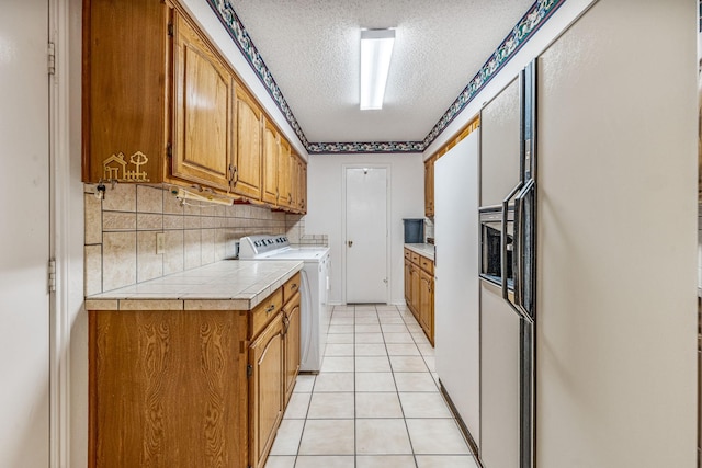 kitchen featuring tile countertops, tasteful backsplash, light tile patterned flooring, a textured ceiling, and independent washer and dryer