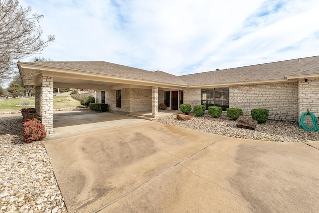 ranch-style home with driveway, an attached carport, roof with shingles, and brick siding