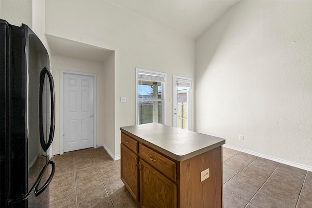 kitchen featuring light tile patterned floors, baseboards, brown cabinets, a center island, and freestanding refrigerator