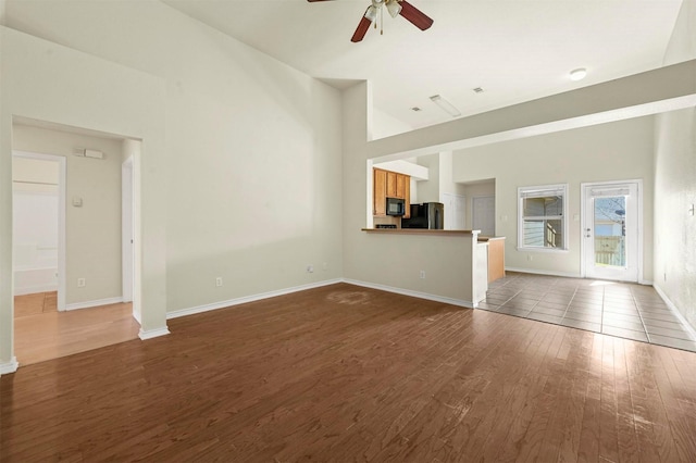 unfurnished living room featuring baseboards, ceiling fan, high vaulted ceiling, and dark wood-style flooring