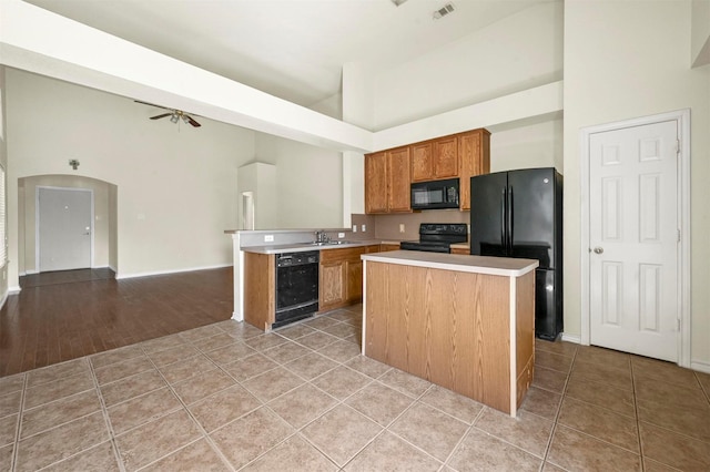 kitchen with black appliances, light tile patterned floors, arched walkways, and light countertops