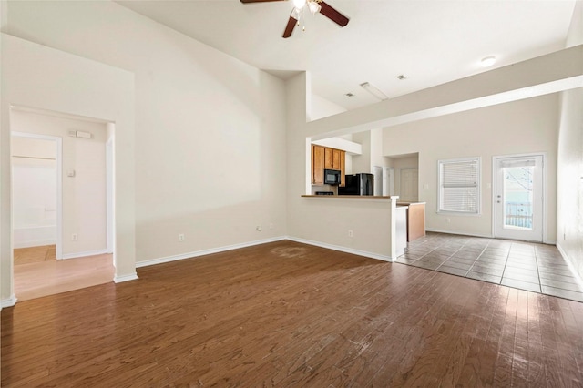 unfurnished living room featuring a ceiling fan, a high ceiling, baseboards, and wood finished floors